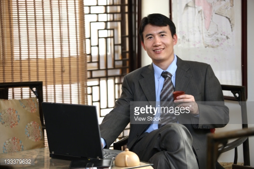 businessman sitting in front of computer desk kick back smile sipping tea pleased.jpg